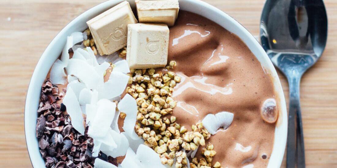 A bowl of food with chocolate, nuts and coconut.