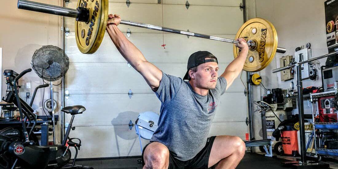 A man squatting with two barbells in his hands.
