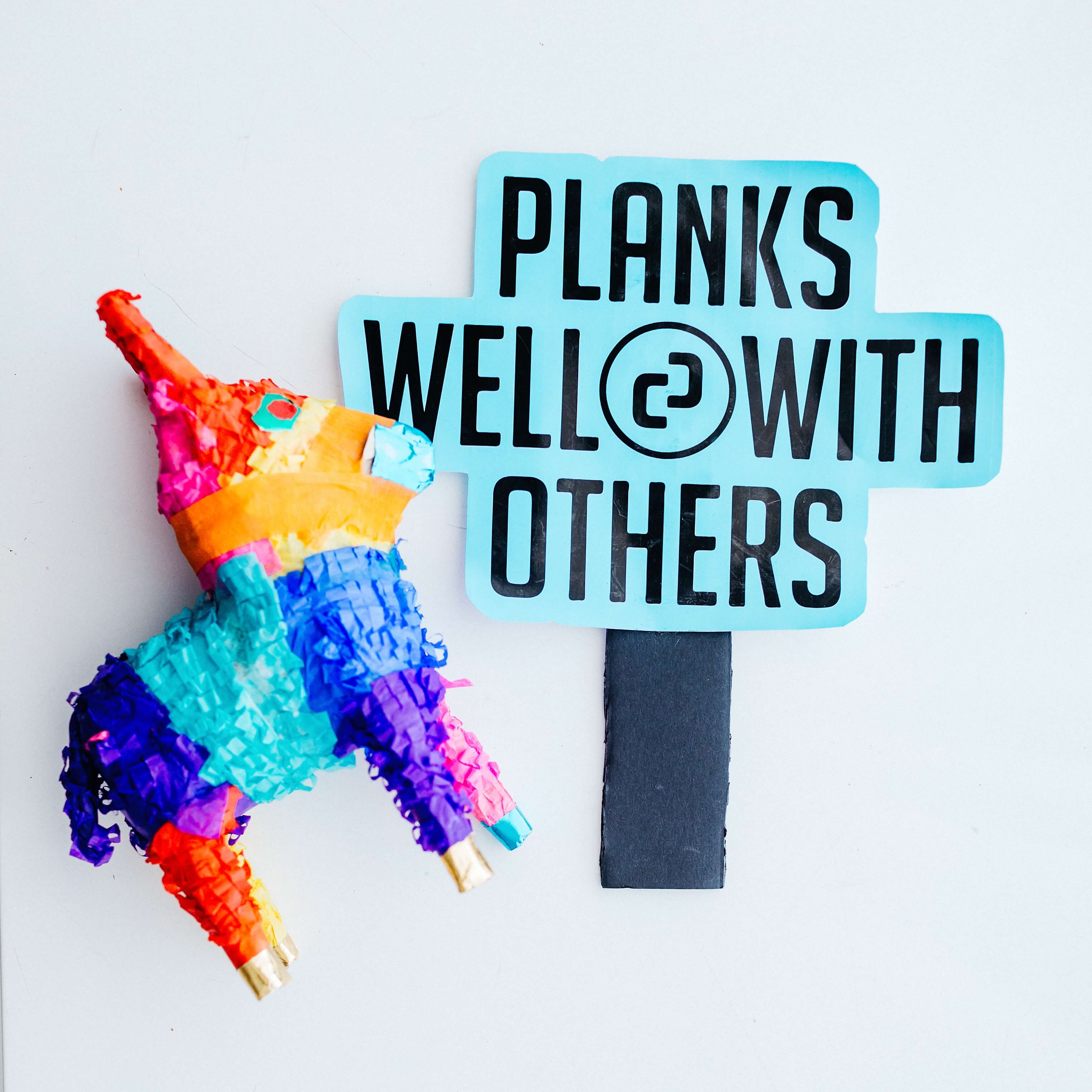 A colorful pinata next to a sign that says planks well with others.